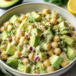 Creamy chickpea and avocado salad served in a bowl garnished with herbs.